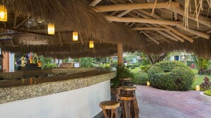 A covered outdoor bar area with a thatched roof, wooden stools, and a stone counter. - Flamingo Vallarta Hotel & Marina (Puerto Vallarta)