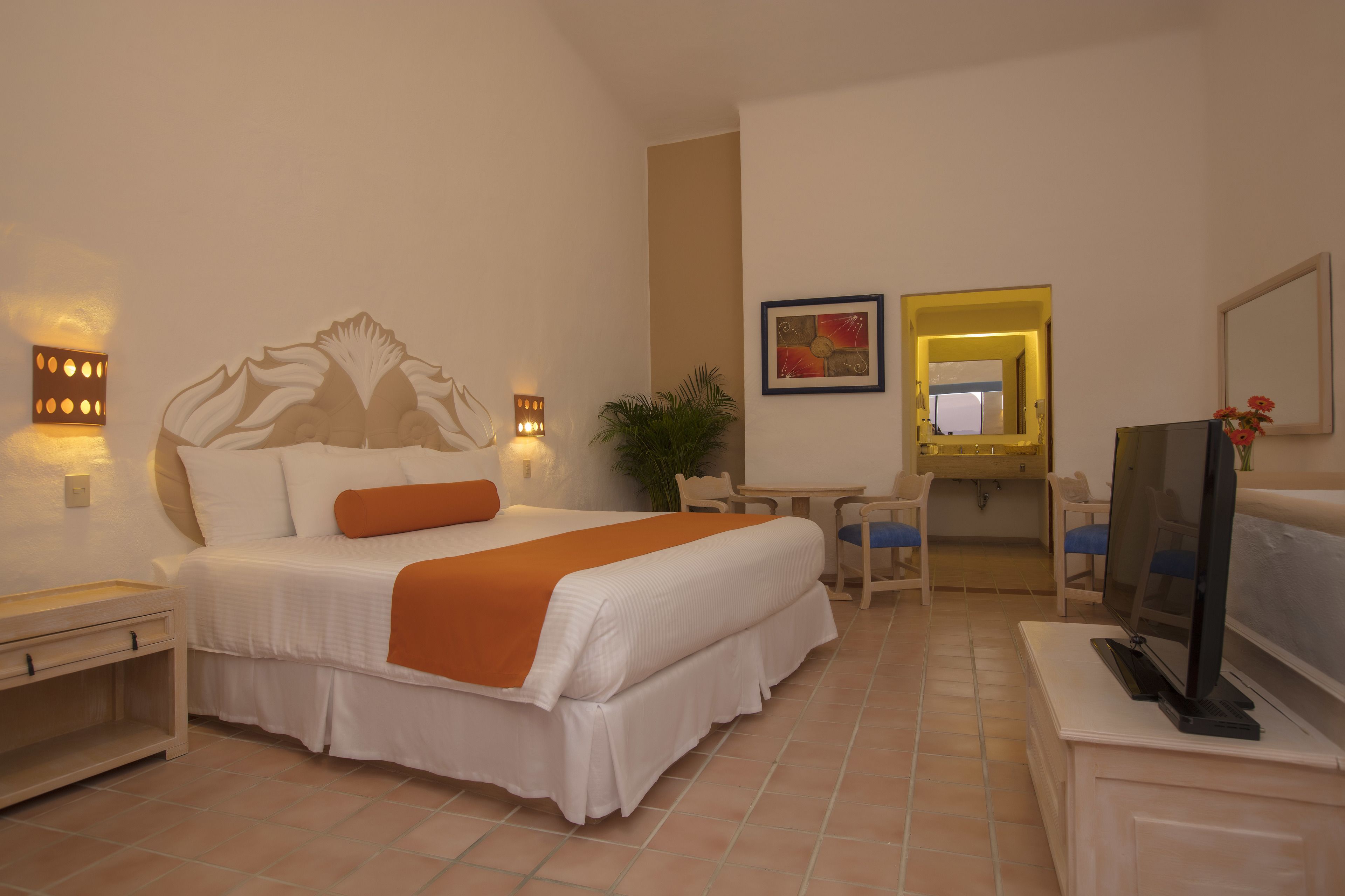 A hotel room with a large bed, a desk, a chair, a television, and a mirror.