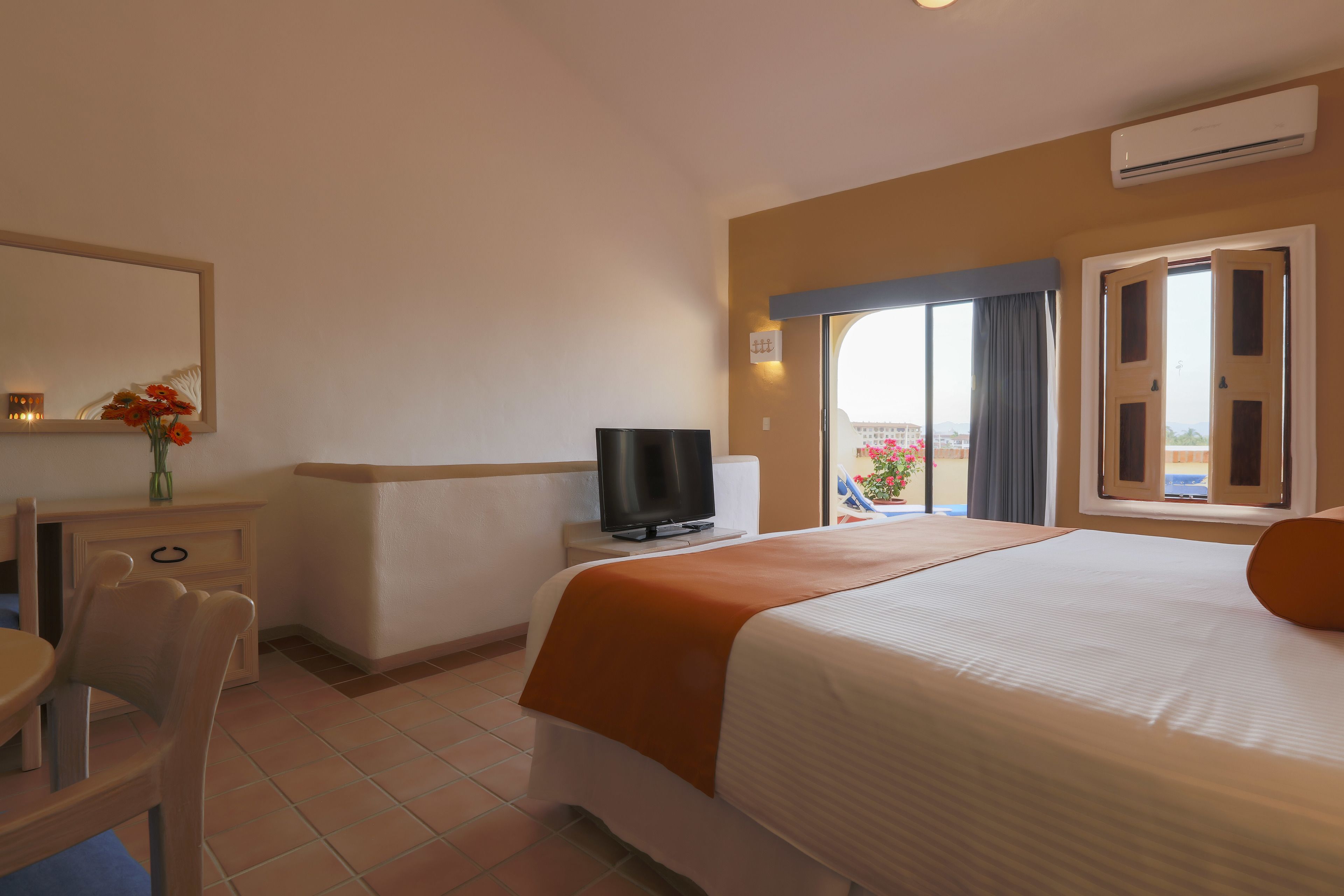 A hotel room with a bed, a television, a desk with a chair, and a window with a view.