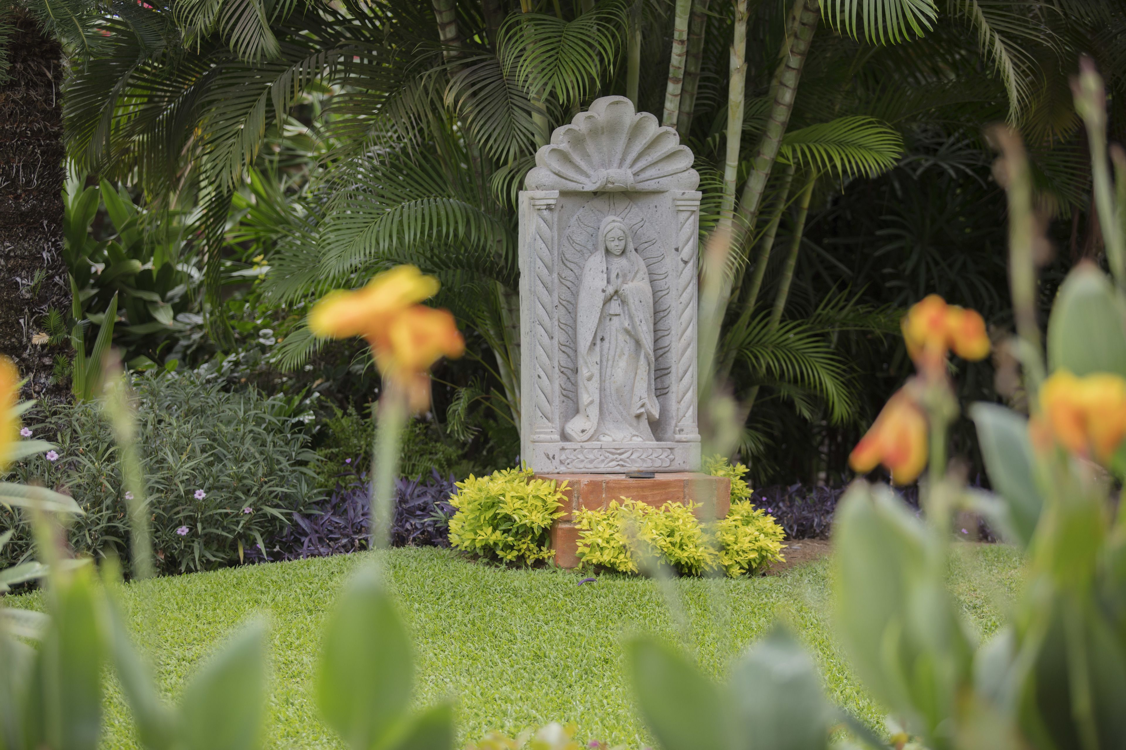 A stone statue in a garden with lush greenery and yellow flowers.