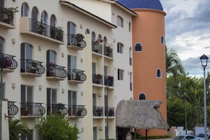 A multi-story hotel with balconies, a thatched-roof structure, and a palm tree in the foreground.