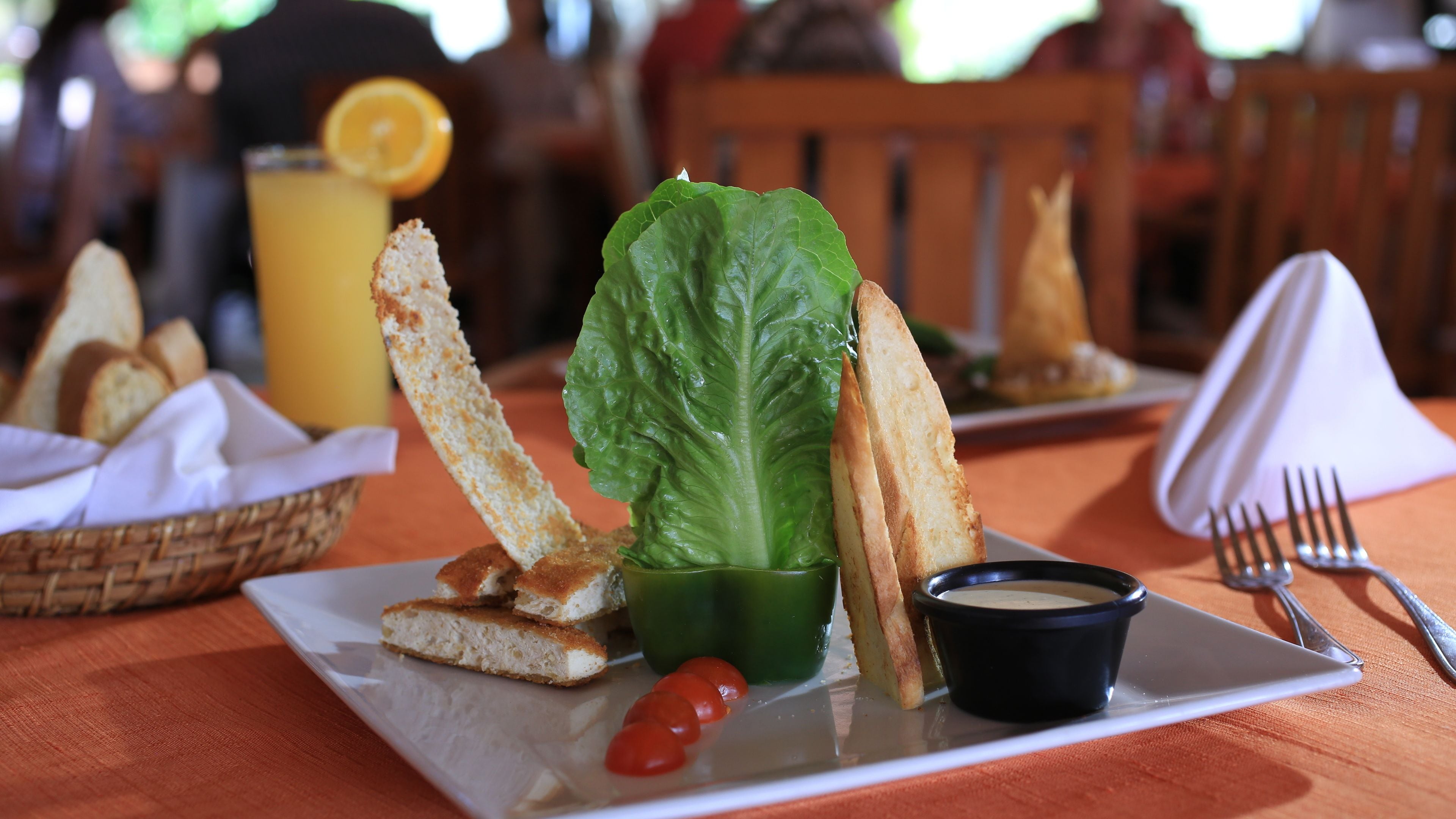 A plate with a salad, bread, and a small bowl of sauce.