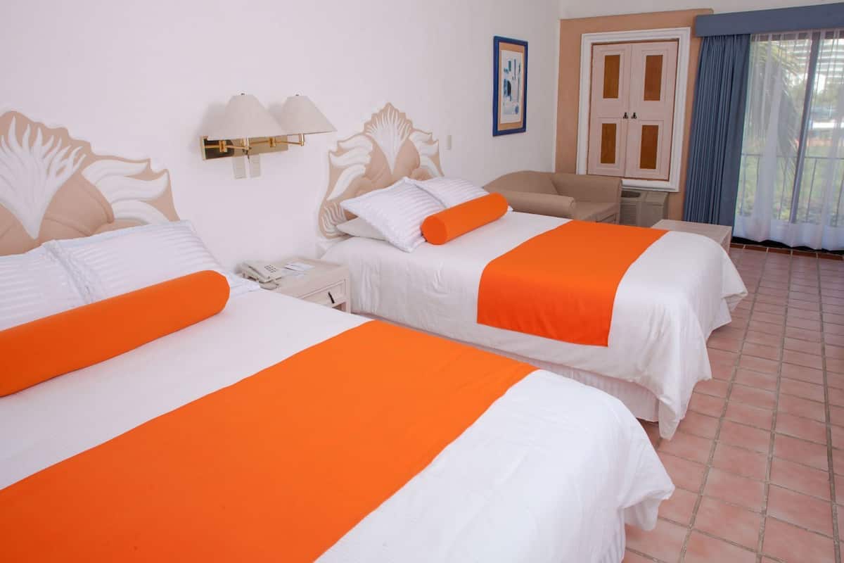Deux lits agrémentés de touches de couleur orange, une chaise, une lampe fixée au mur et une porte avec un rideau bleu.