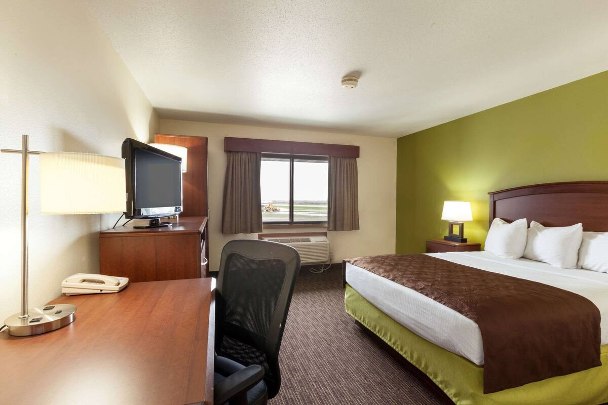 A hotel room with a bed, desk, chair, television, and a window with curtains.