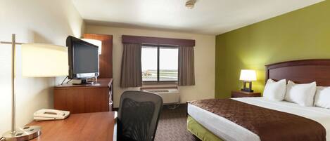A hotel room with a bed, desk, chair, television, and a window with curtains.
