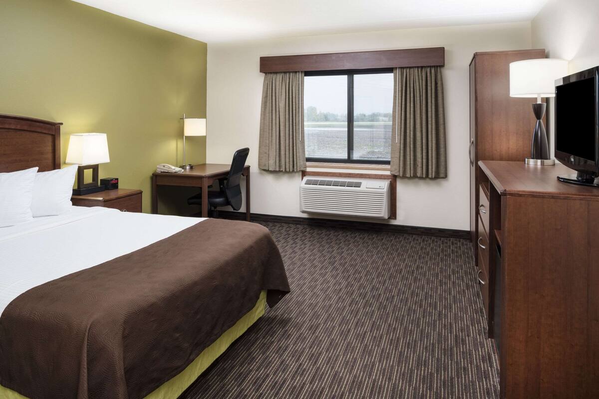 A hotel room with a large bed, a desk, a chair, a television, and a window with curtains.