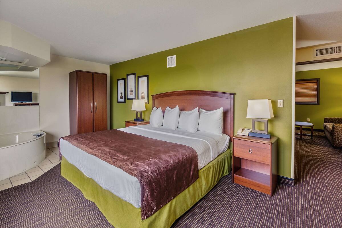 A hotel room with a bed, a nightstand, a lamp, a television, a wardrobe, and a bathroom.