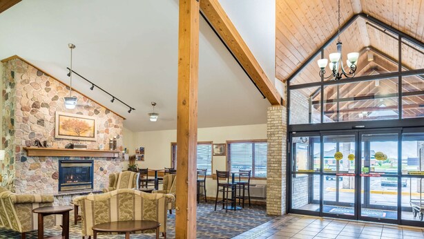 A lobby with a stone wall, fireplace, seating area, and large windows. - AmericInn by Wyndham Wahpeton (Wahpeton)