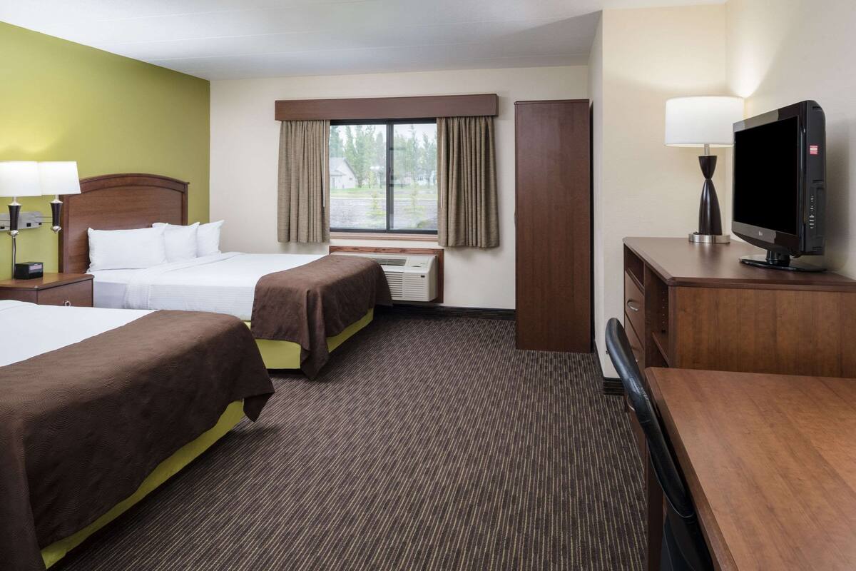 A hotel room with two beds, a desk, a television, and a window with curtains.