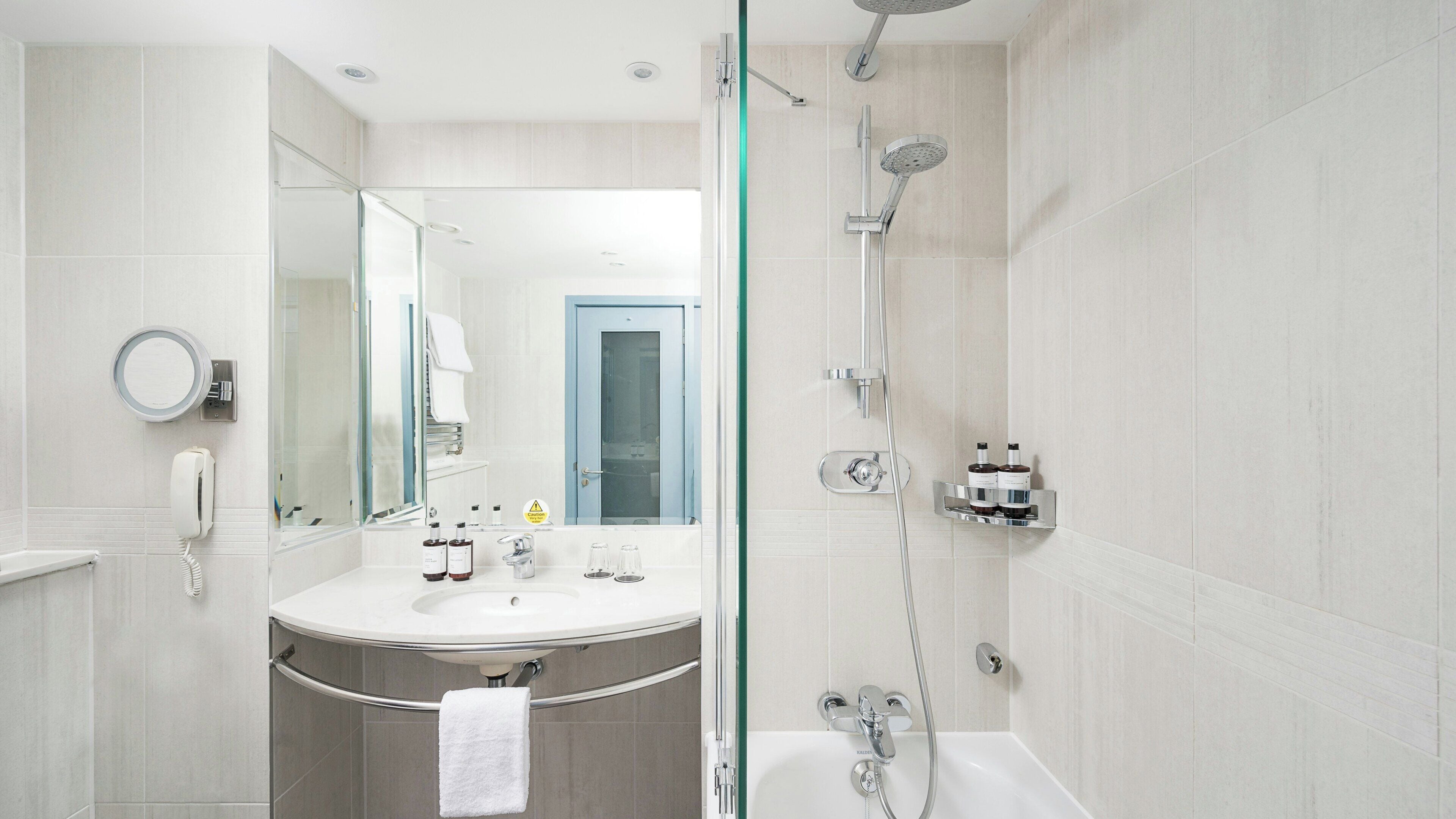 A modern bathroom with a glass-enclosed shower, a round mirror, a white sink, and a visible door.