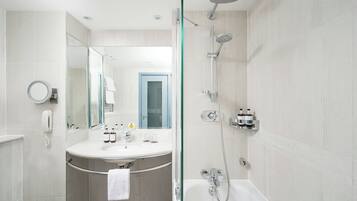 A modern bathroom with a glass-enclosed shower, a round mirror, a white sink, and a visible door.