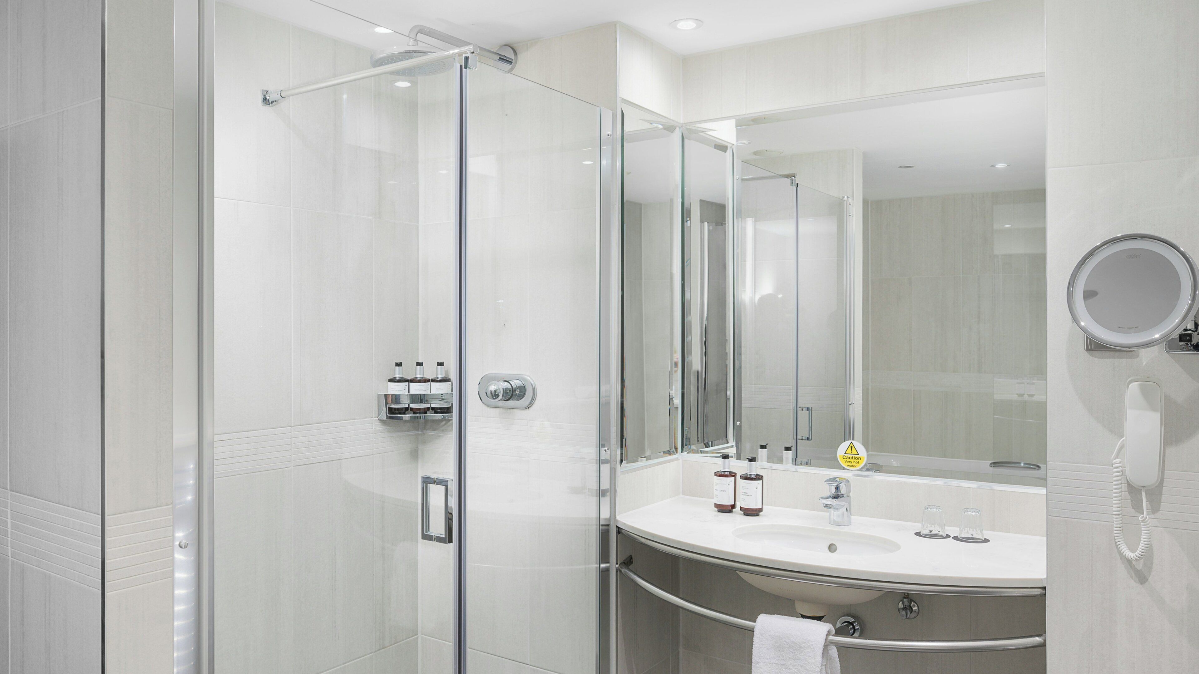 A modern bathroom with a glass-enclosed shower, a vanity with a large mirror, and a built-in telephone.