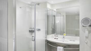 A modern bathroom with a glass-enclosed shower, a vanity with a large mirror, and a built-in telephone.