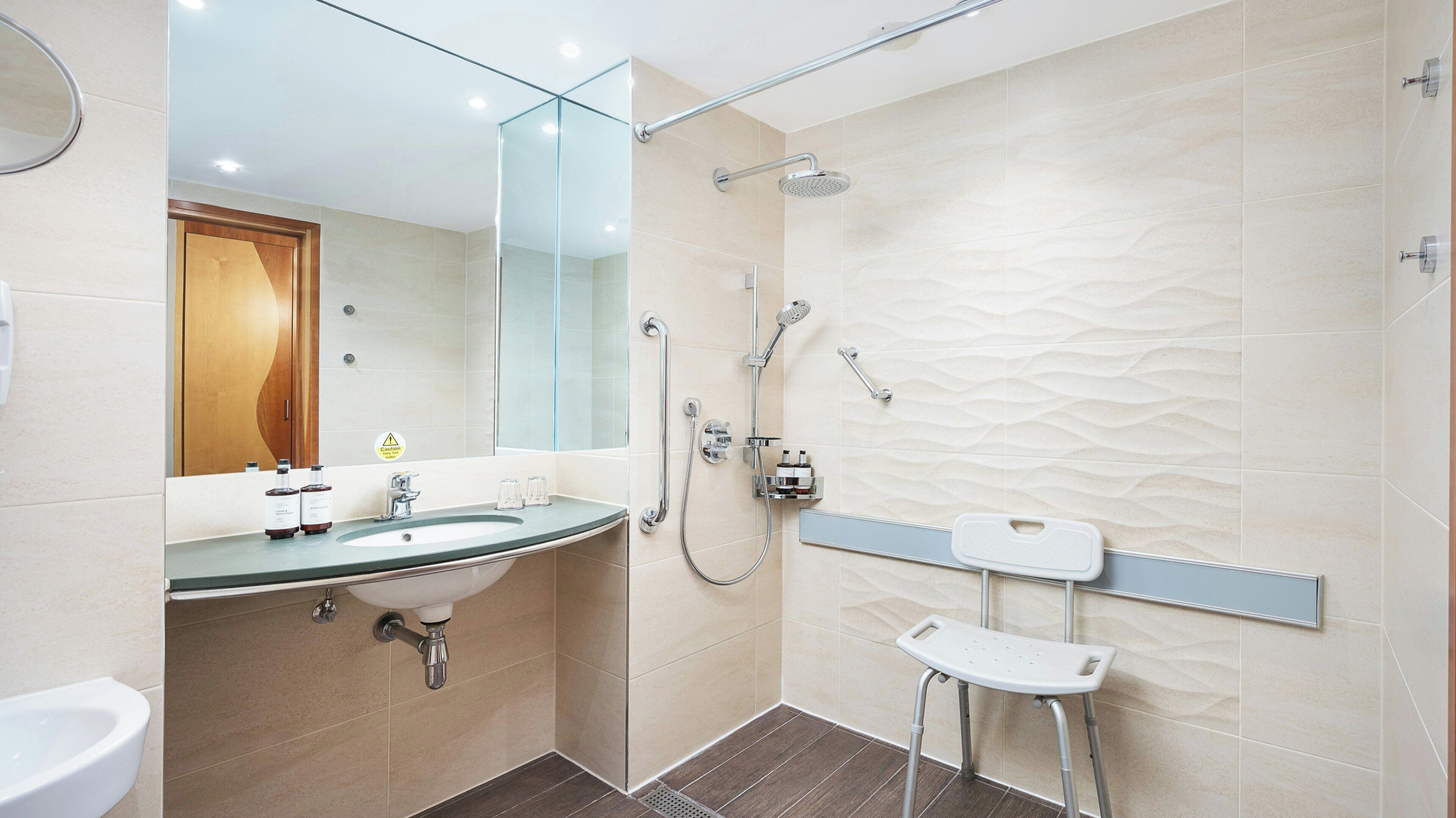 Un baño moderno con un lavamanos de vidrio, una ducha con cabezal de ducha manual y un inodoro con barra de apoyo.