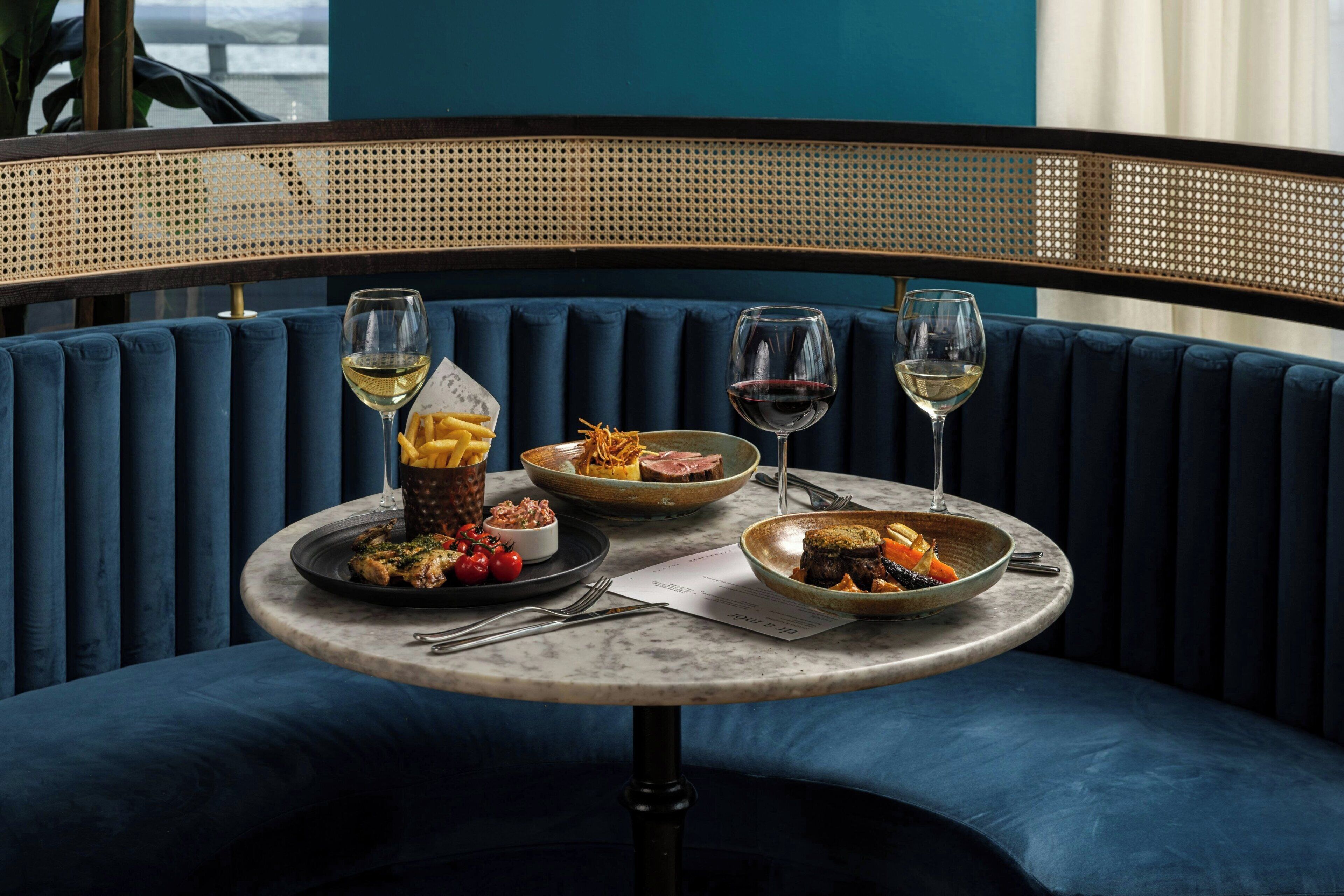Comedor con una mesa redonda preparada para dos personas, con platos de comida, copas de vino y cubiertos.