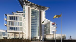 Un bâtiment moderne doté d’une façade en verre incurvée, de nombreux drapeaux et d’une structure de toit particulière.
