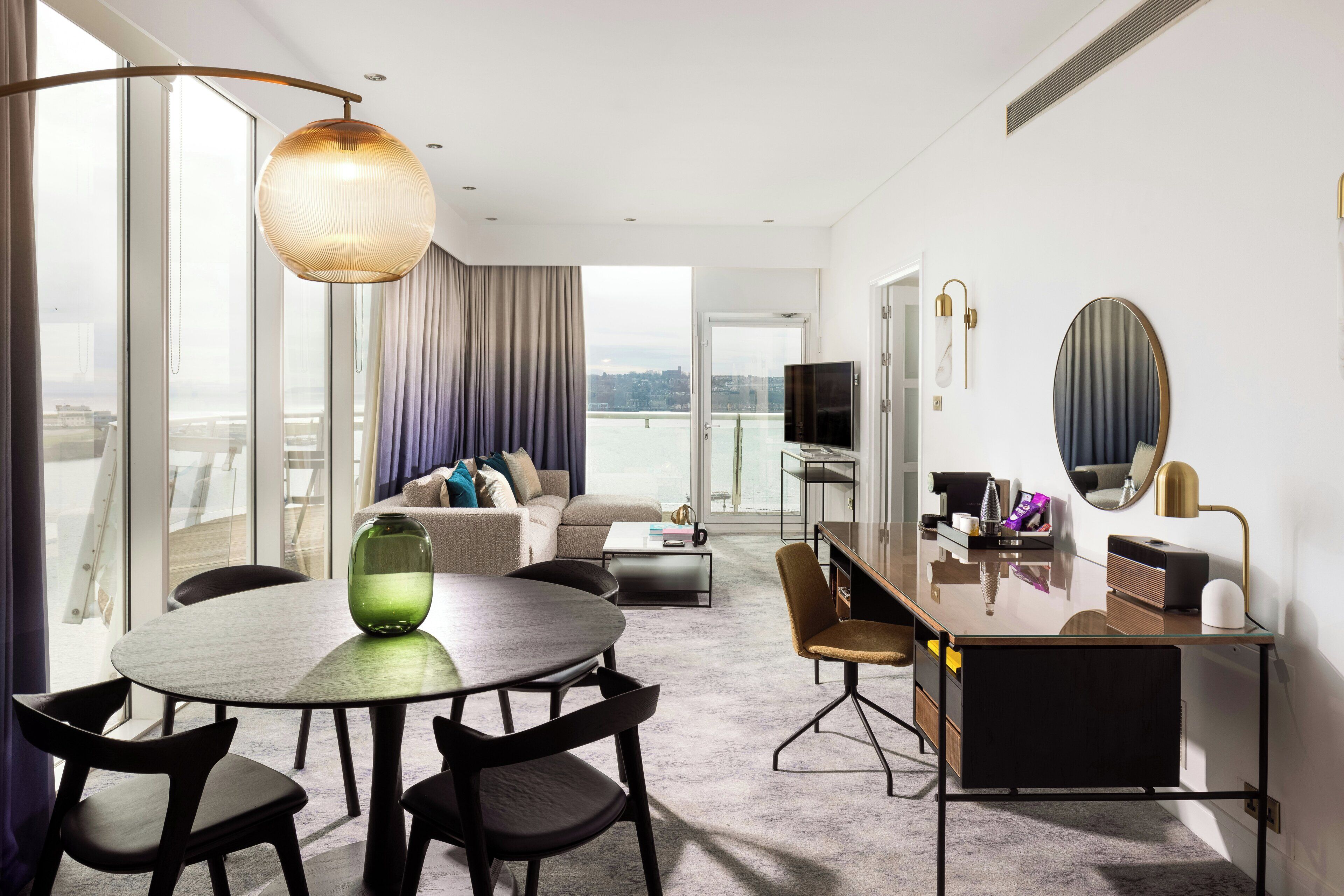Una habitación de hotel moderna con comedor, sofá, televisor y balcón con vistas.