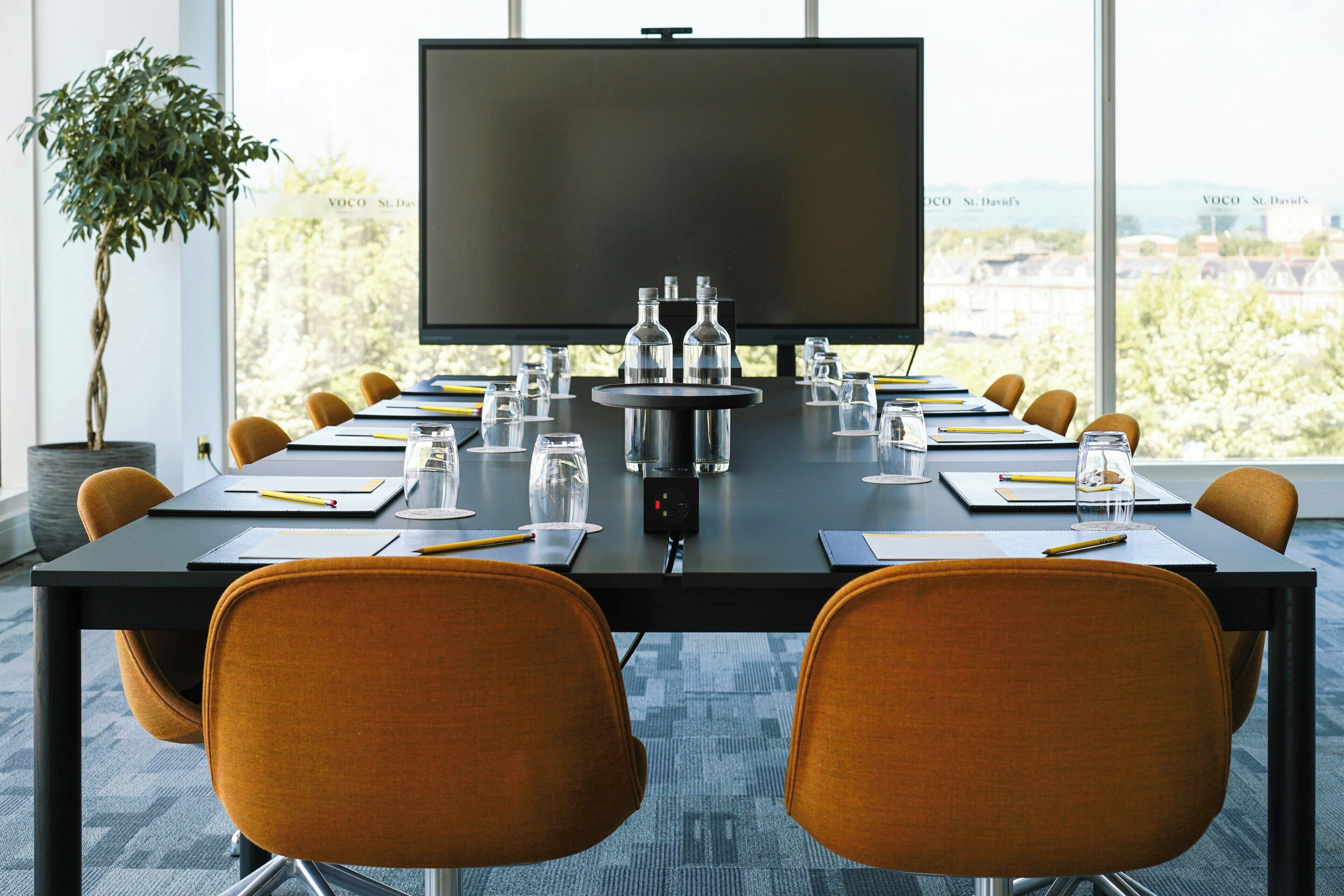 A conference room with a large screen, multiple chairs, water bottles, and glasses on the table.
