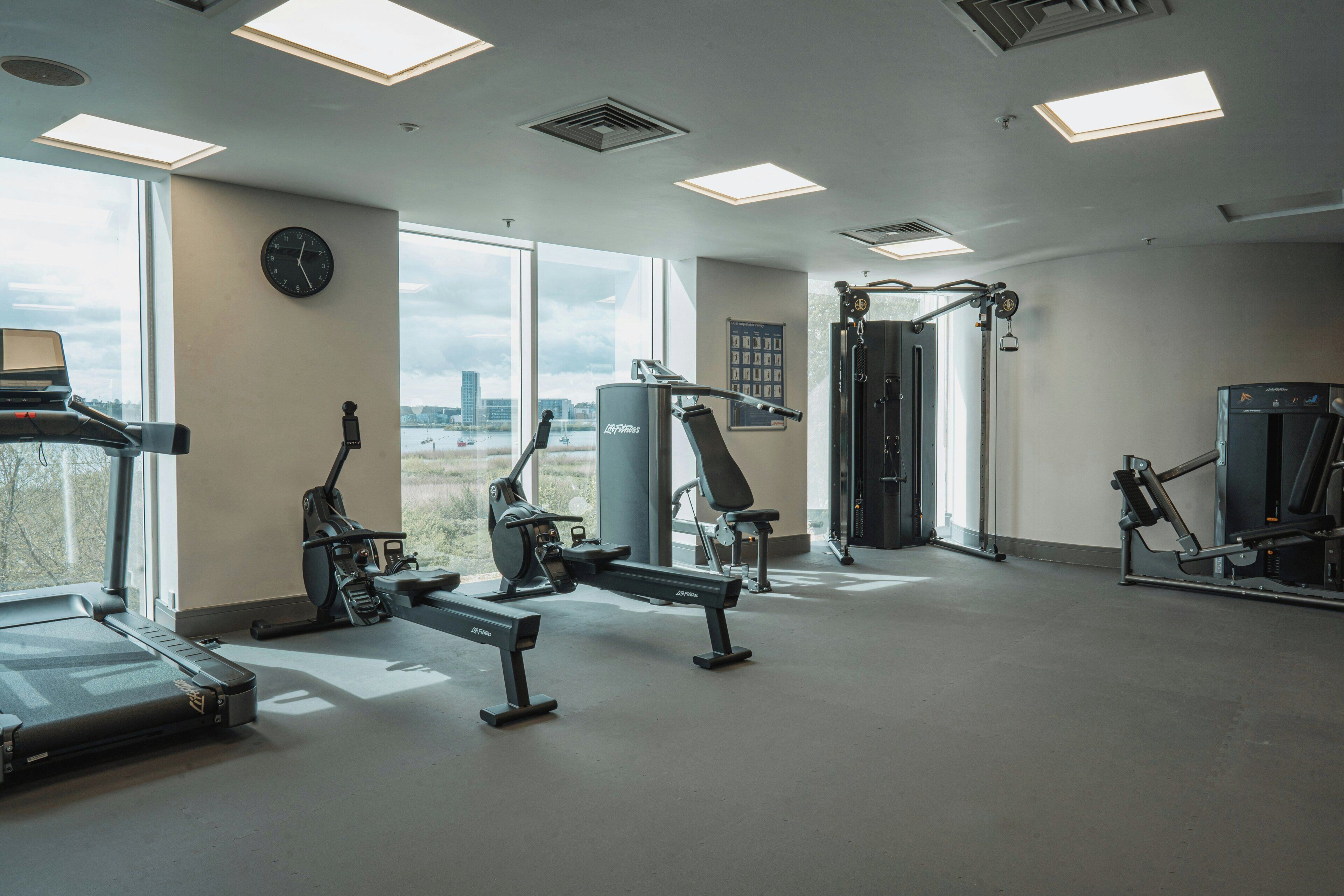 Une salle de sport équipée de machines de cardio, de matériel de musculation et de grandes fenêtres donnant sur la ville.