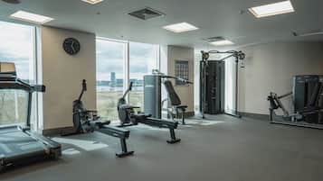 Une salle de sport équipée de machines de cardio, de matériel de musculation et de grandes fenêtres donnant sur la ville.