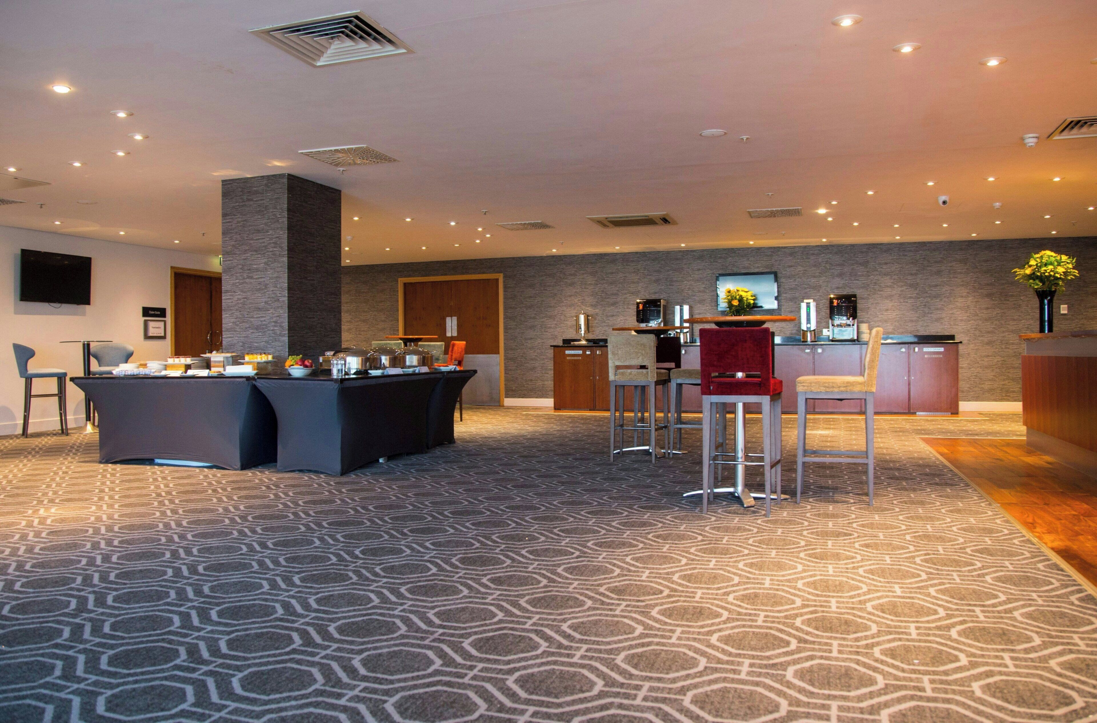 Un vestíbulo moderno de hotel con zona de bar, asientos y alfombra estampada.