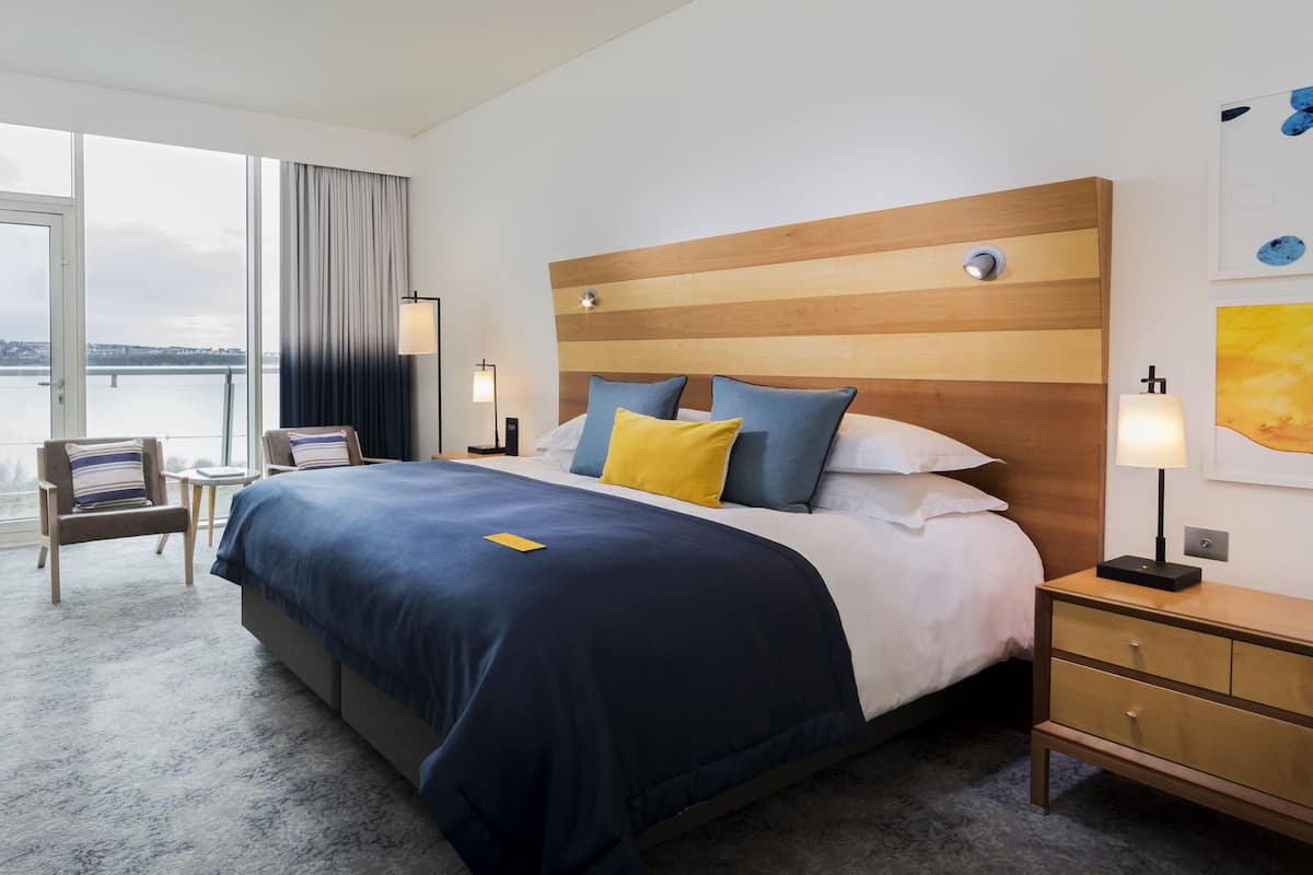 Habitación de hotel moderna con una cama grande, vistas a un cuerpo de agua y un cabecero de madera.