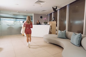 A reception area with a modern design, including a reception desk, a sofa with cushions, and a decorative plant. - voco St David's Cardiff by IHG (Cardiff)