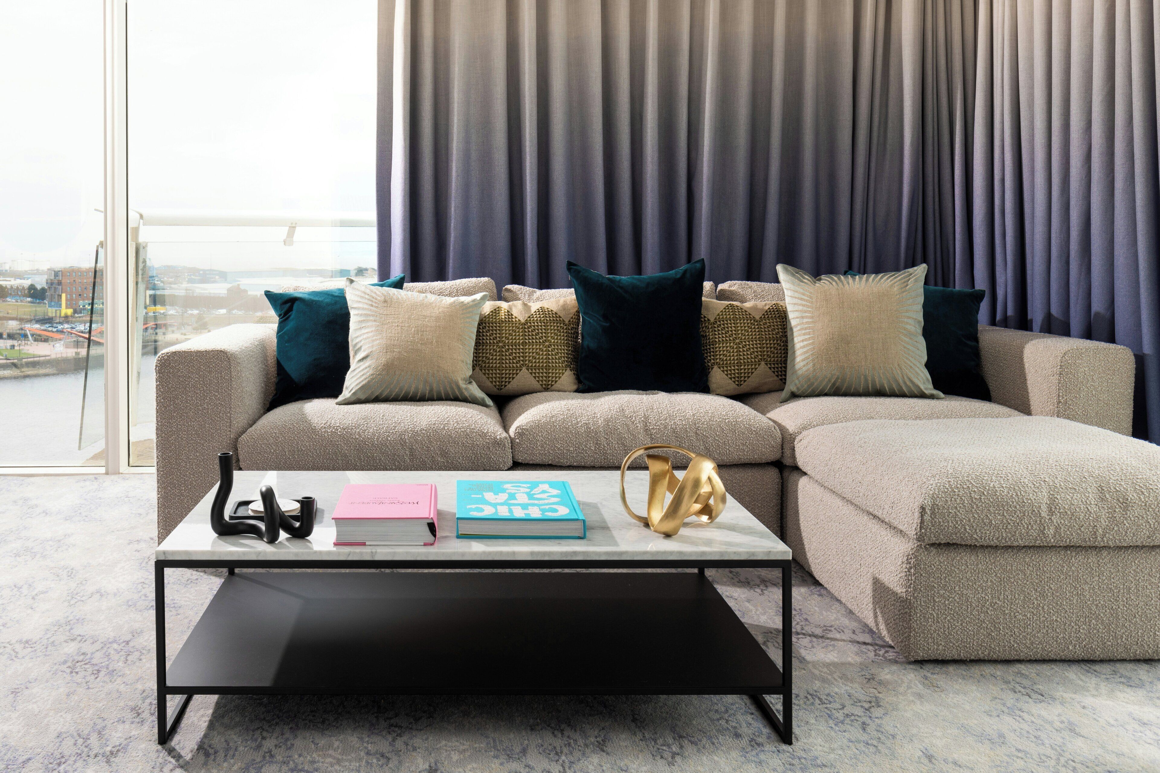 A modern living room with a sectional sofa, a coffee table, and a view of a cityscape through large windows.