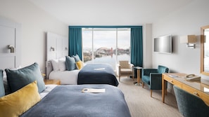 A hotel room with two beds, a desk, a chair, a TV, and a view of a cityscape through large windows. - voco St David's Cardiff by IHG (Cardiff)