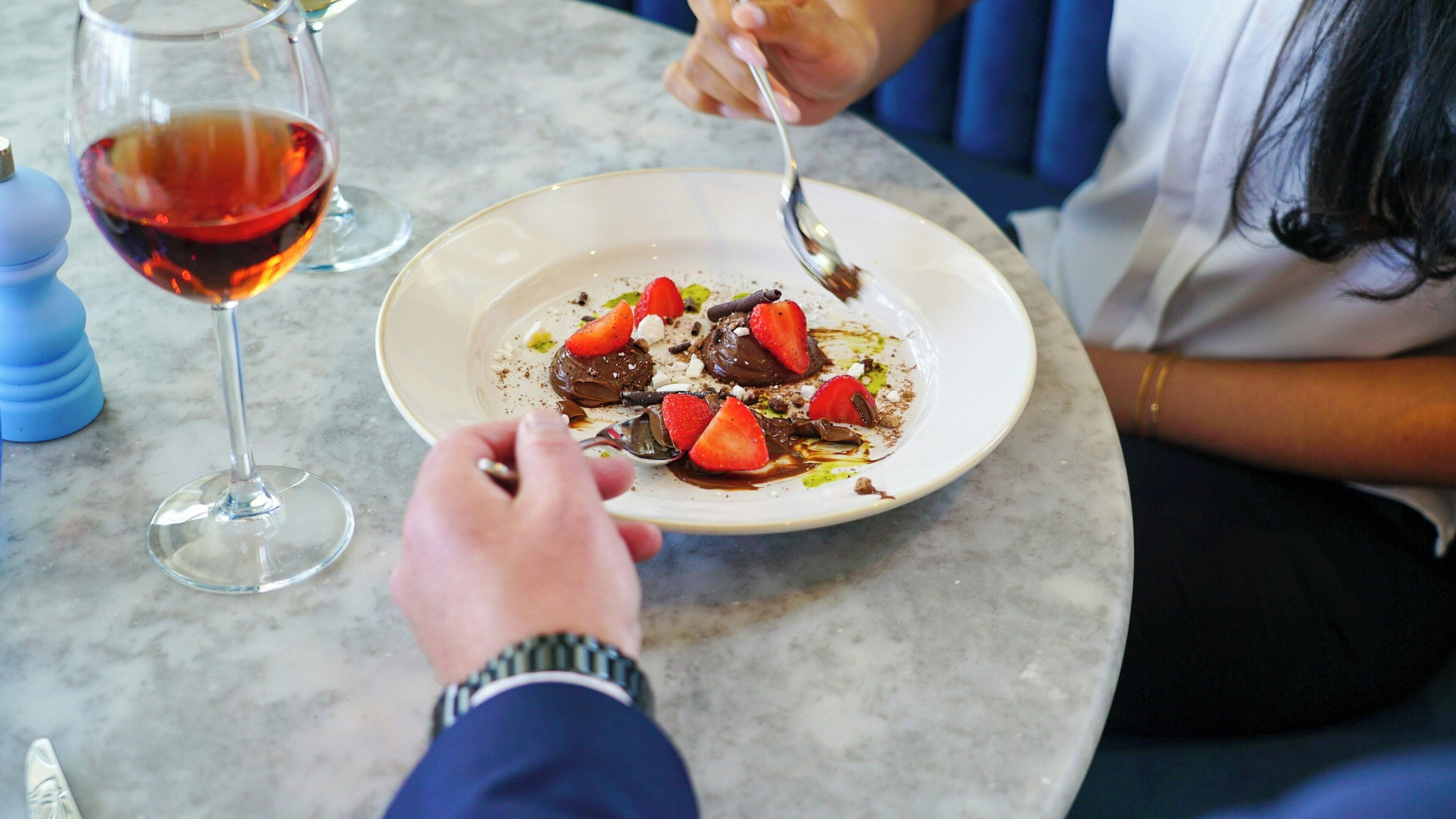 A dining table with a plate of food, a wine glass, and a person eating.