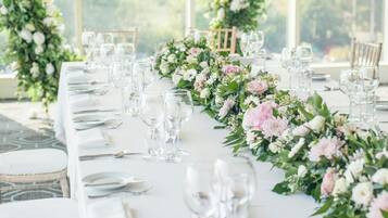 A table set for a formal event with clear glassware and white tablecloths, surrounded by floral arrangements.
