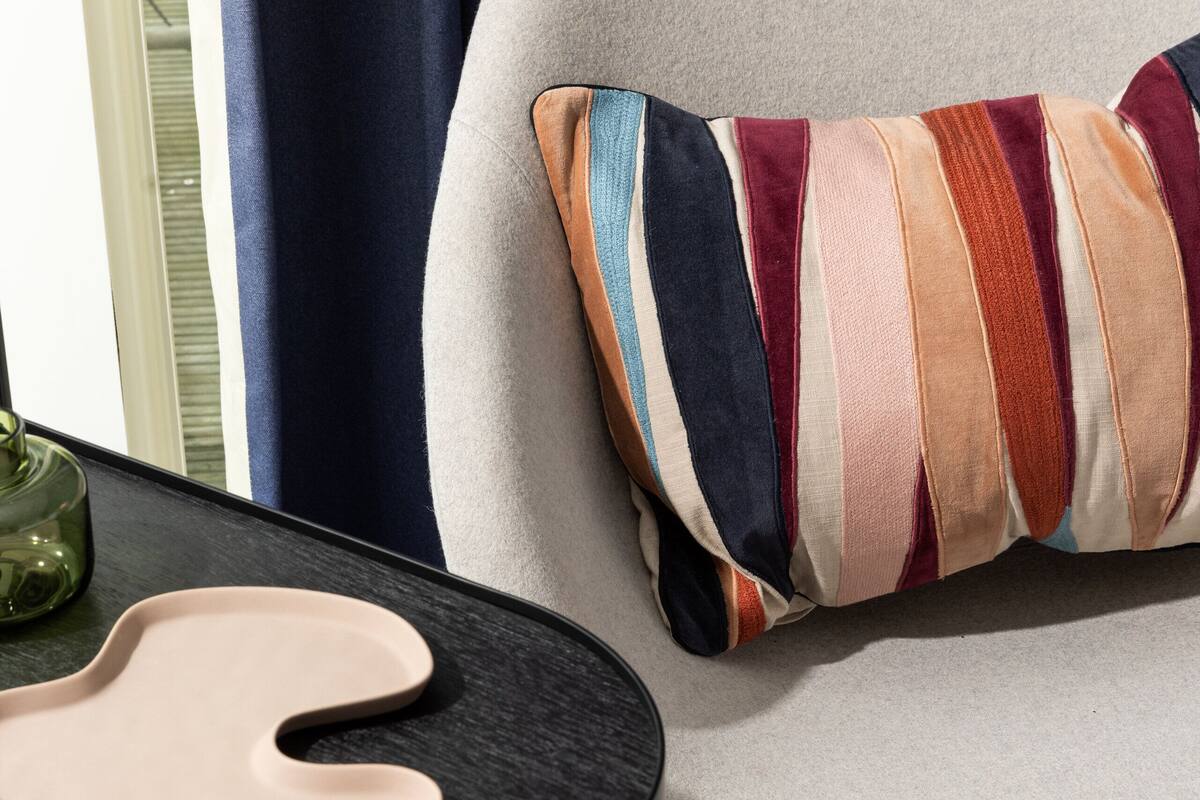 Una habitación moderna con un sillón gris, un cojín a rayas coloridos, una mesita de noche negra y un jarrón verde.