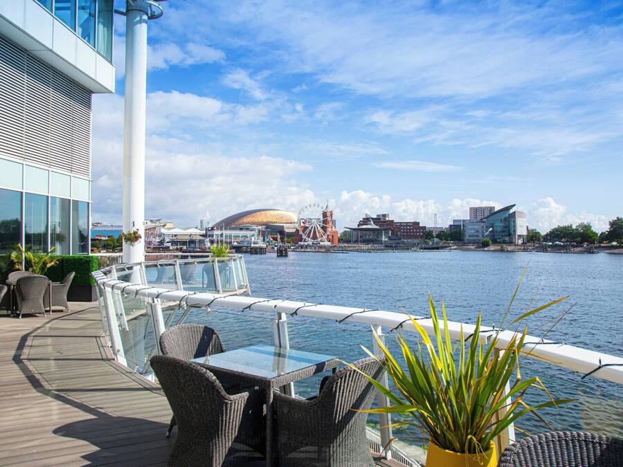 Terraza con mobiliario de mimbre con vista a un cuerpo de agua y edificios al fondo.