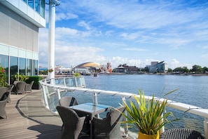 A deck with wicker furniture overlooking a body of water with buildings in the background. - voco St David's Cardiff by IHG (Cardiff)
