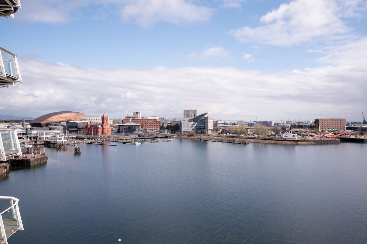 A waterfront cityscape with modern buildings, a large dome structure, and a calm river.