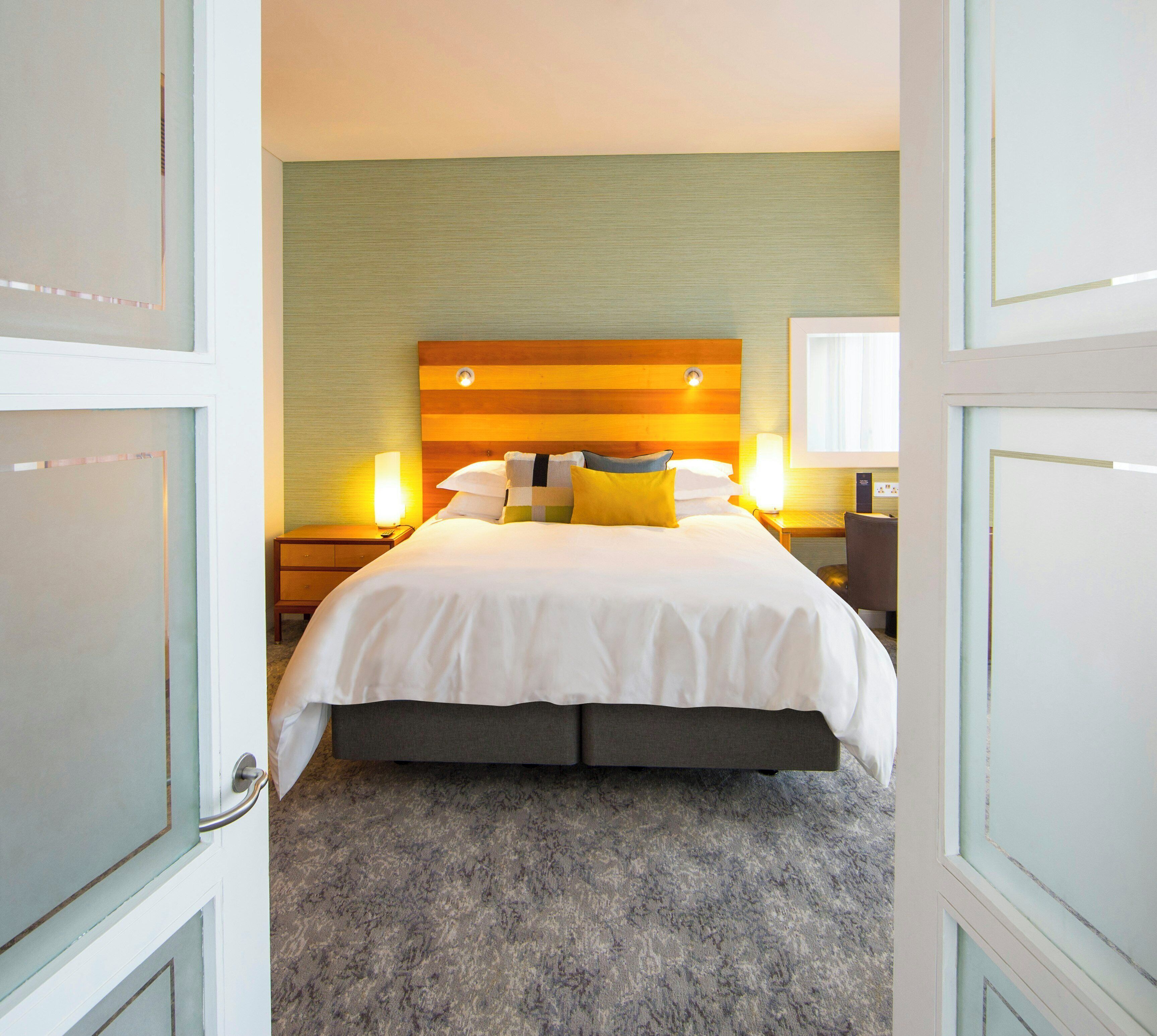 A hotel room with a bed, bedside lamps, and a view through an open door.