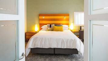 A hotel room with a bed, bedside lamps, and a view through an open door.