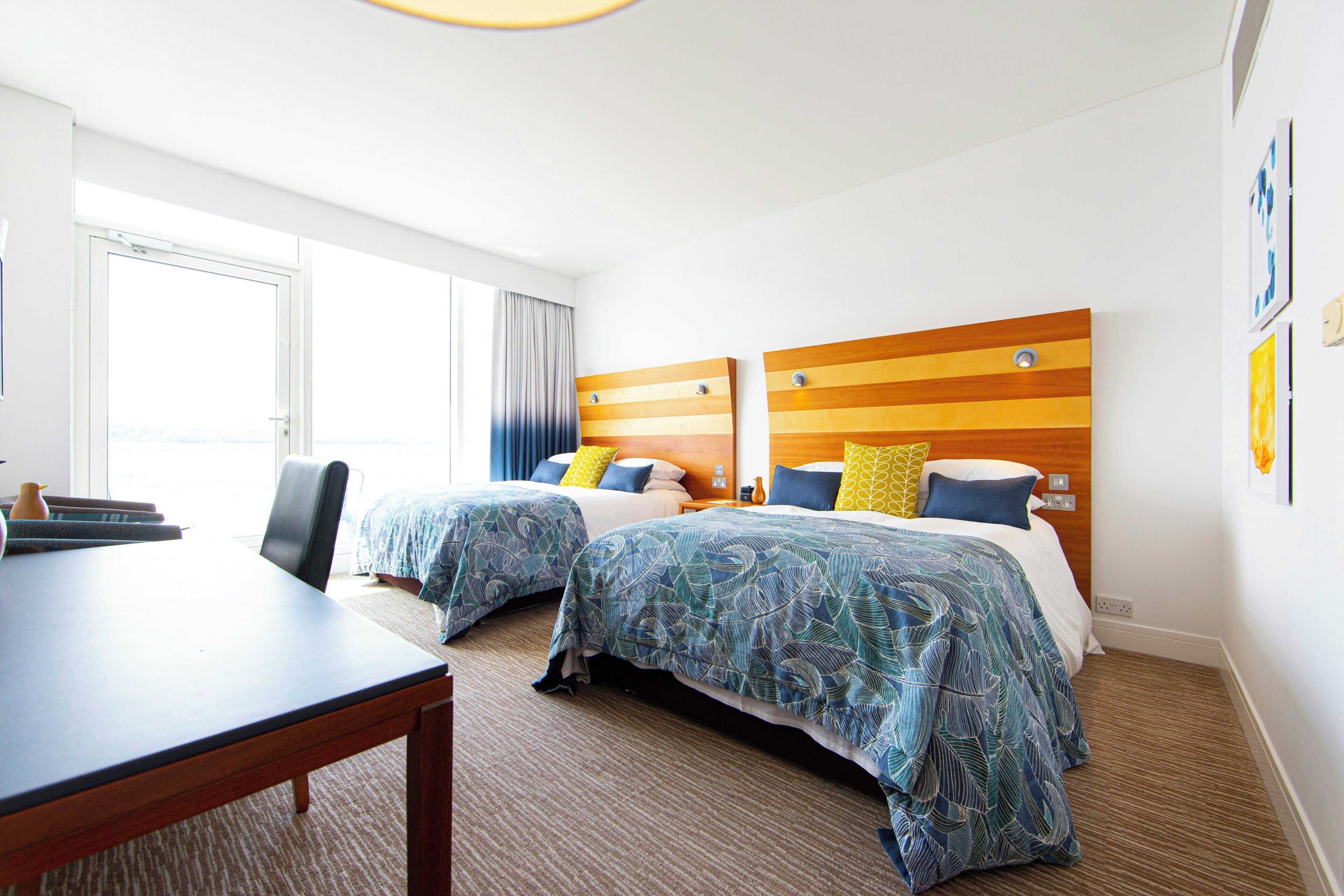 A hotel room with two beds, a desk, and a large window.