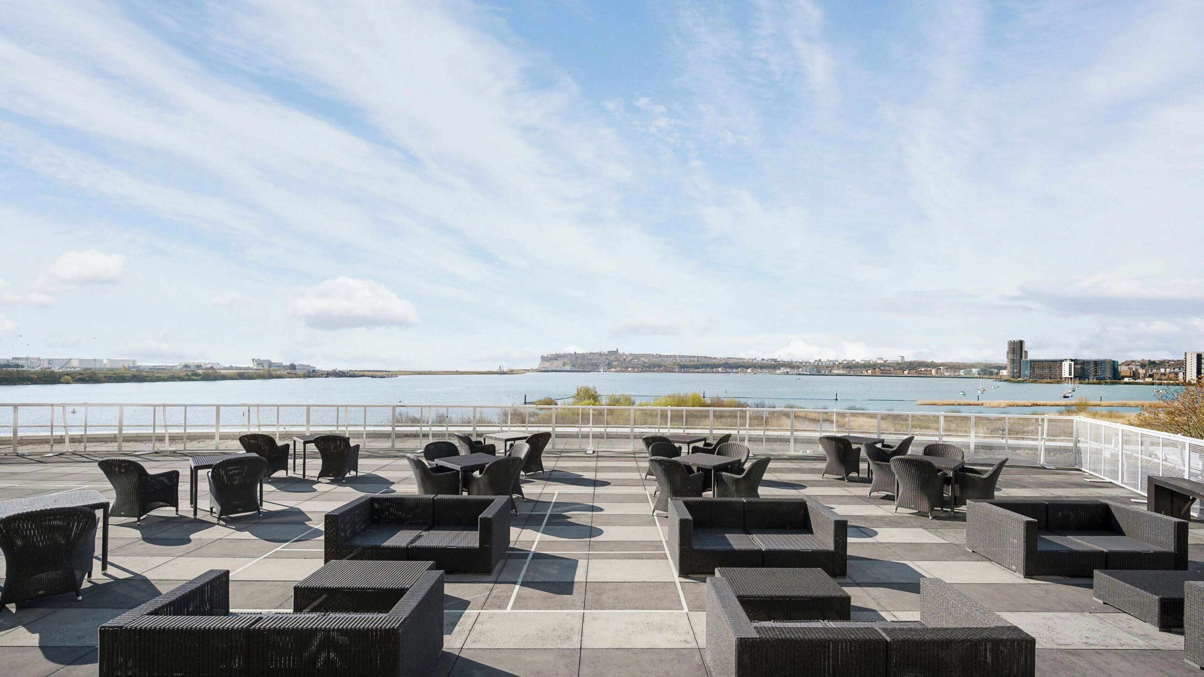 An outdoor seating area with wicker furniture and a view of a body of water and distant buildings.