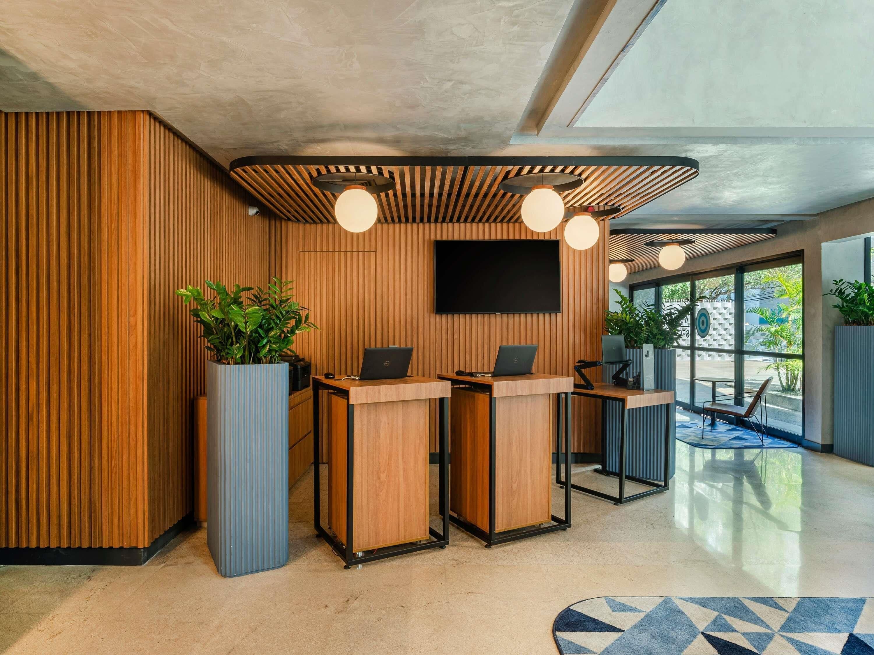 A modern reception area with wooden paneling, a flat-screen TV, and two reception desks with laptops.