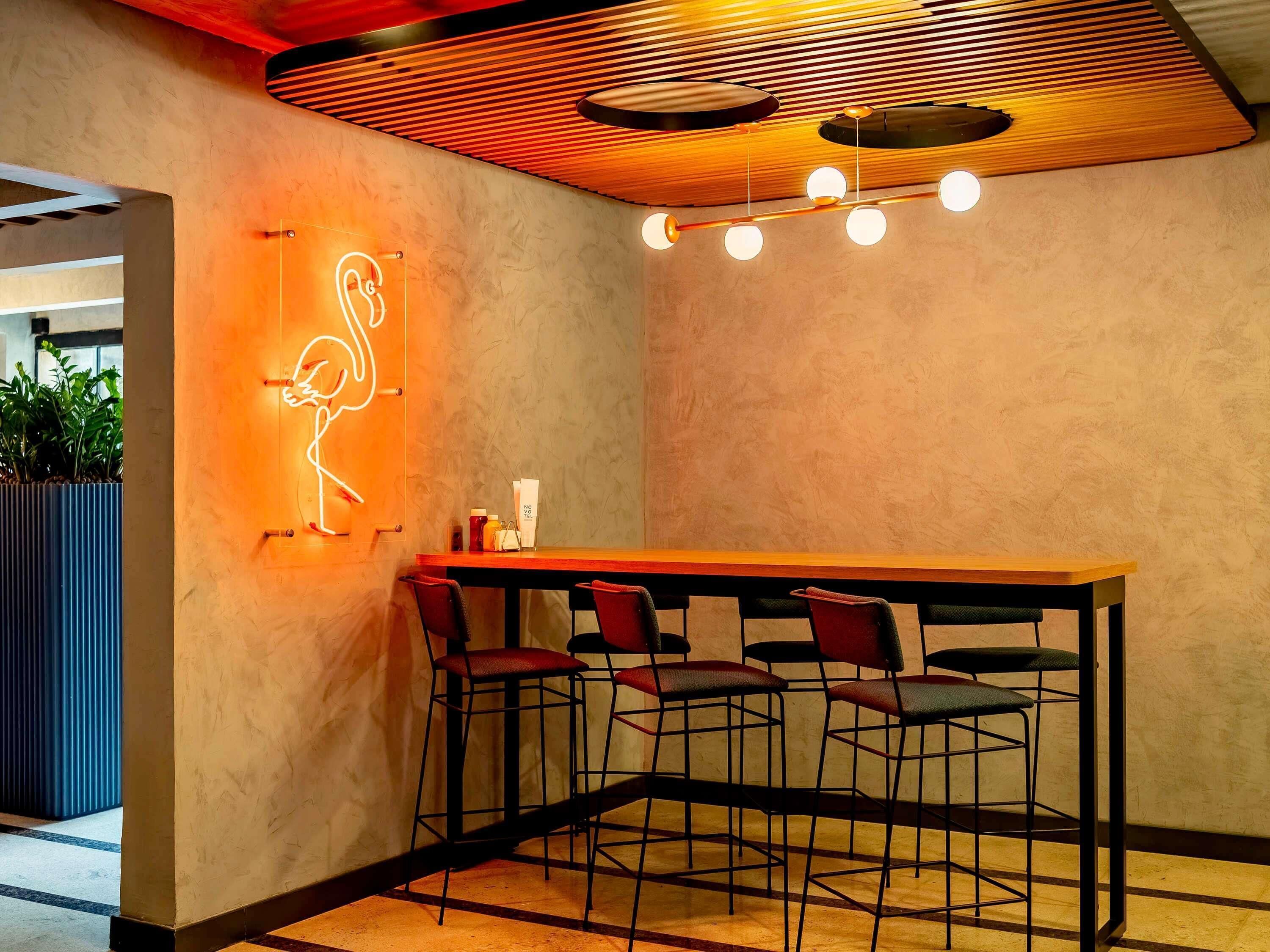 A bar area with a neon flamingo sign, a wooden ceiling, and a bar counter with stools.