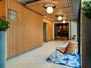 Um interior moderno com parede de ripas de madeira, balcão de recepção e área de estar com tapete de padrão geométrico.