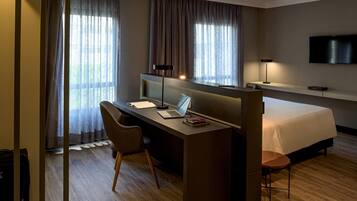 A hotel room with a desk, chair, bed, and a TV mounted on the wall.