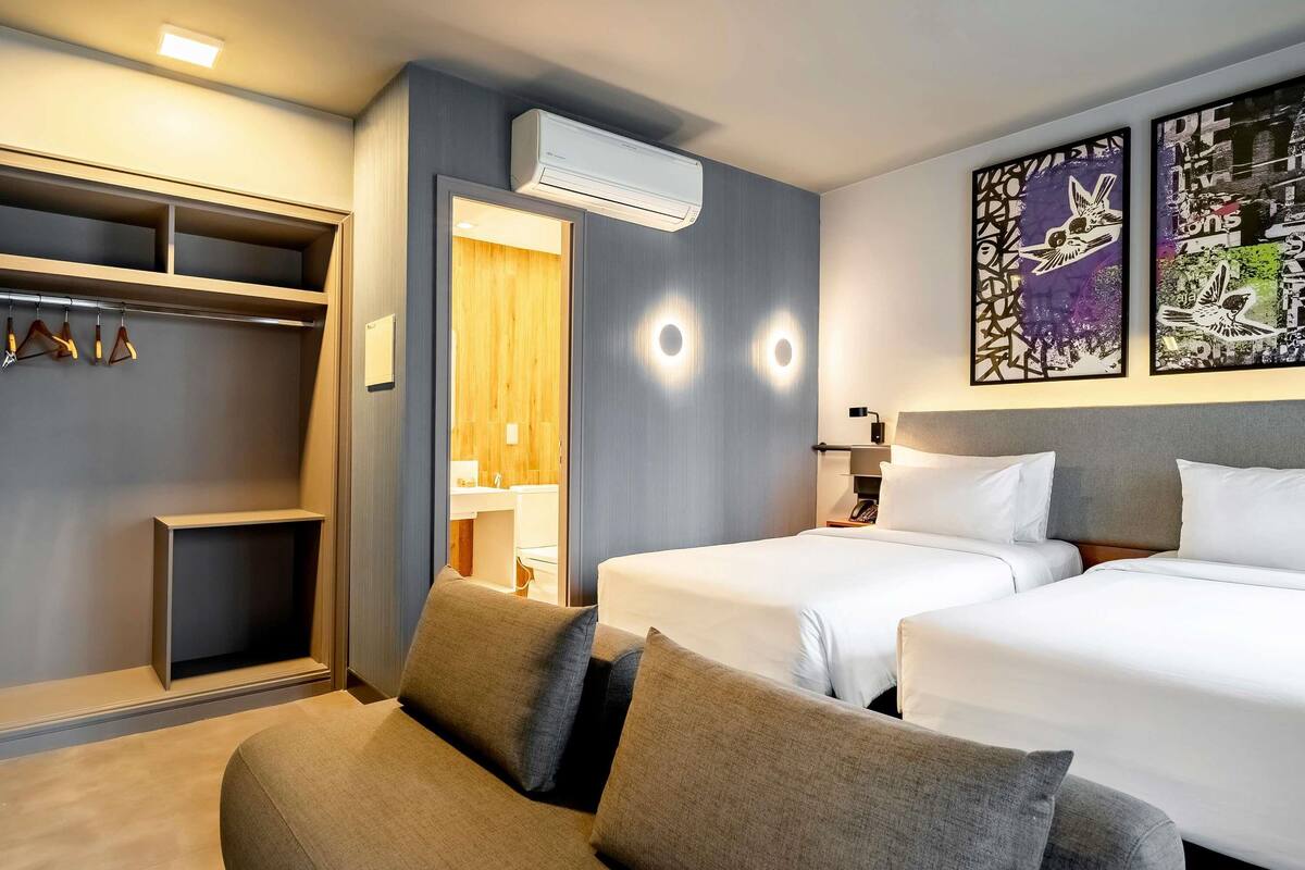 Ein Hotelzimmer mit zwei Betten, einem Schlafsofa, einem Kleiderschrank und einem durchgegangenen Badezimmer.