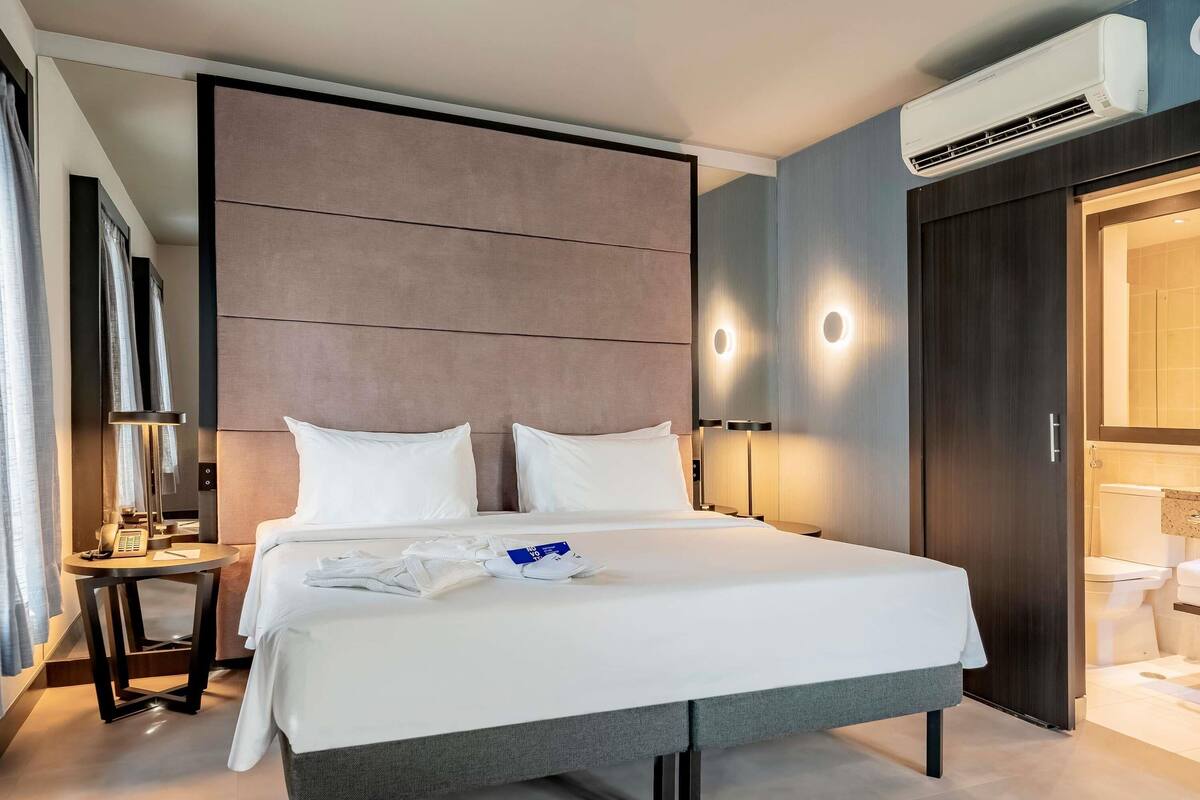 Ein modernes Hotelzimmer mit einem großen Bett, einem Nachttisch, einer Lampe und einer Klimaanlage.