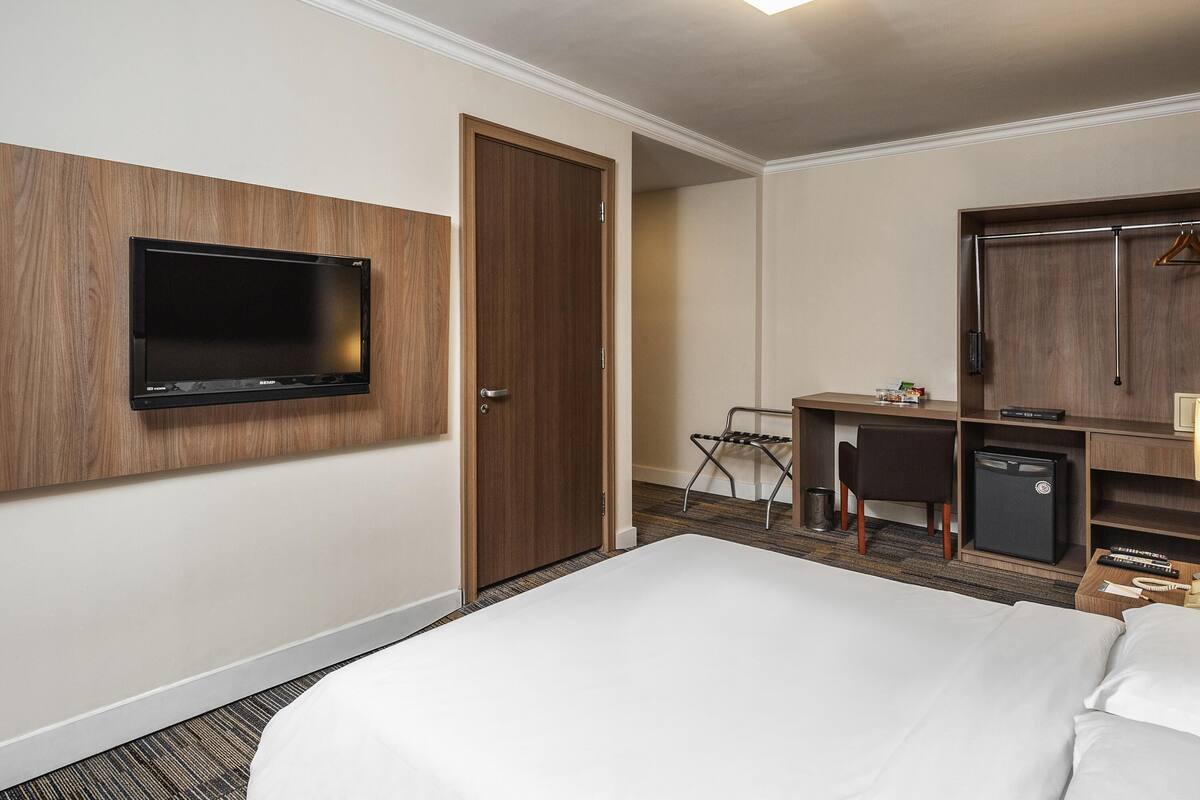 Ein Hotelzimmer mit Bett, Schreibtisch, Fernseher, Kleiderschrank und kleinem Kühlschrank.