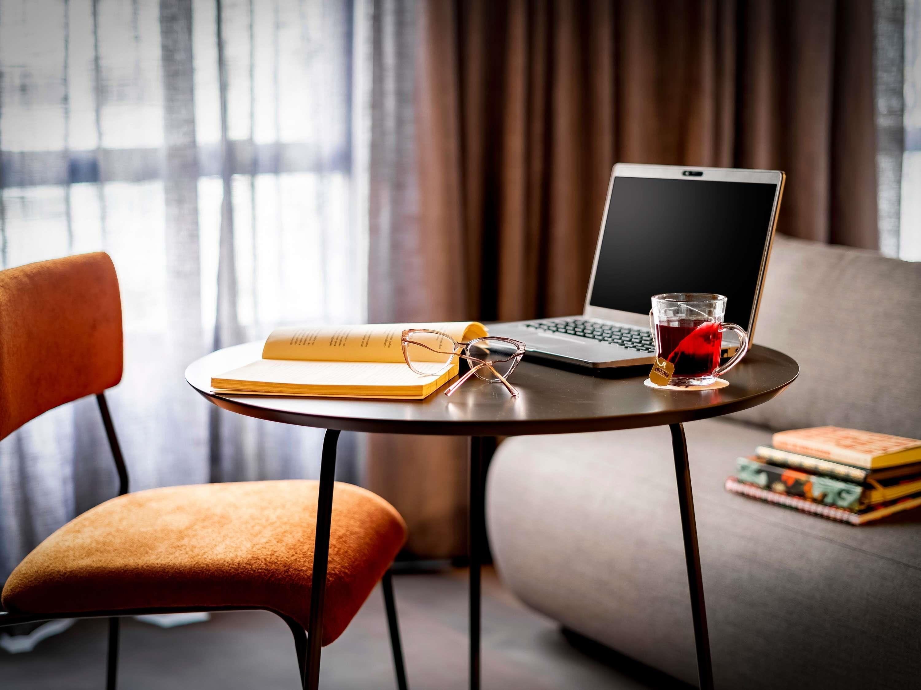 Una computadora portátil sobre una mesa redonda con un libro, gafas y una taza de té.