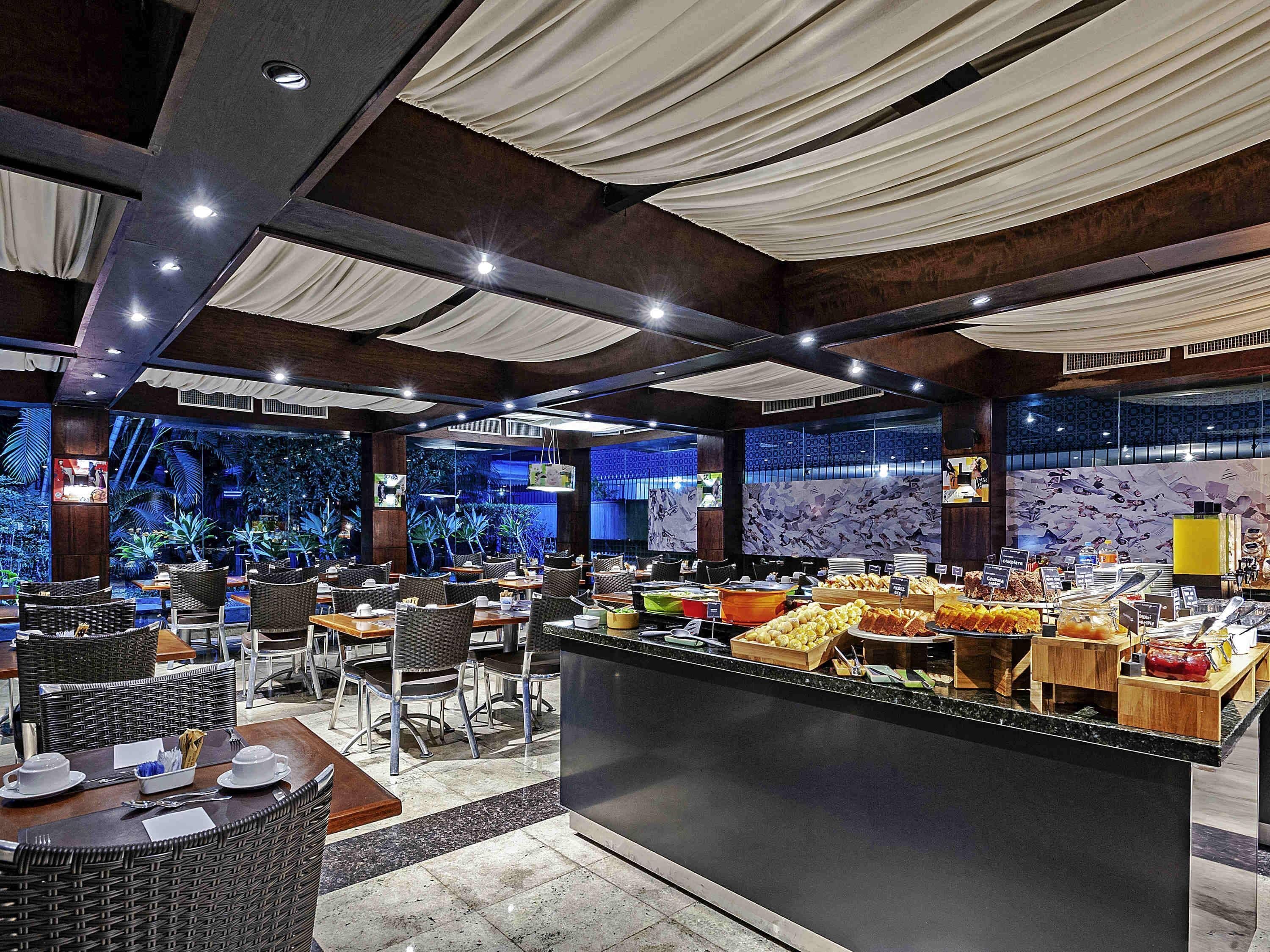 A restaurant with a buffet, wicker furniture, and a tropical-themed wall.