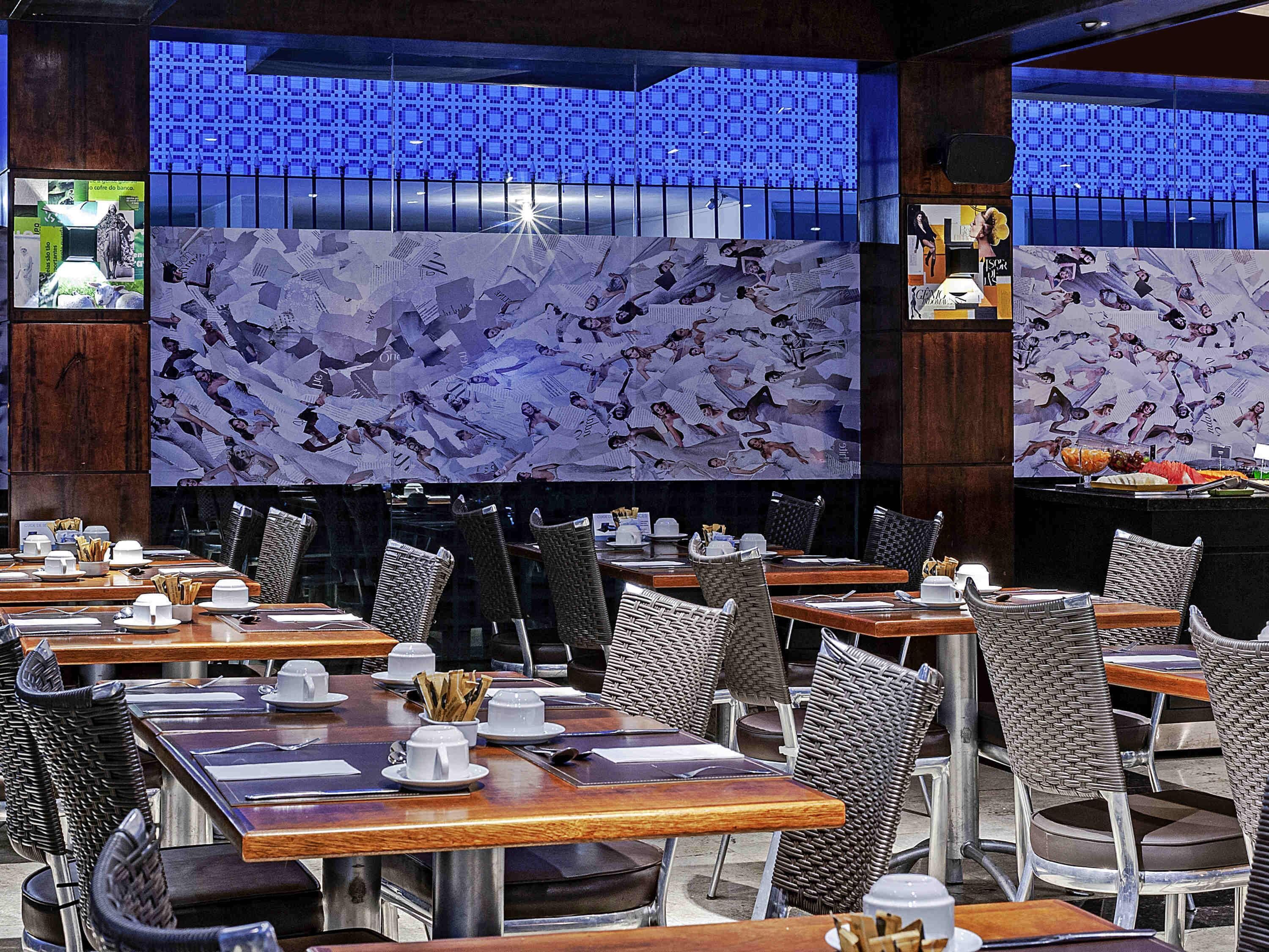 A restaurant interior with multiple dining tables and chairs, a patterned wall, and a blue-lit backdrop.