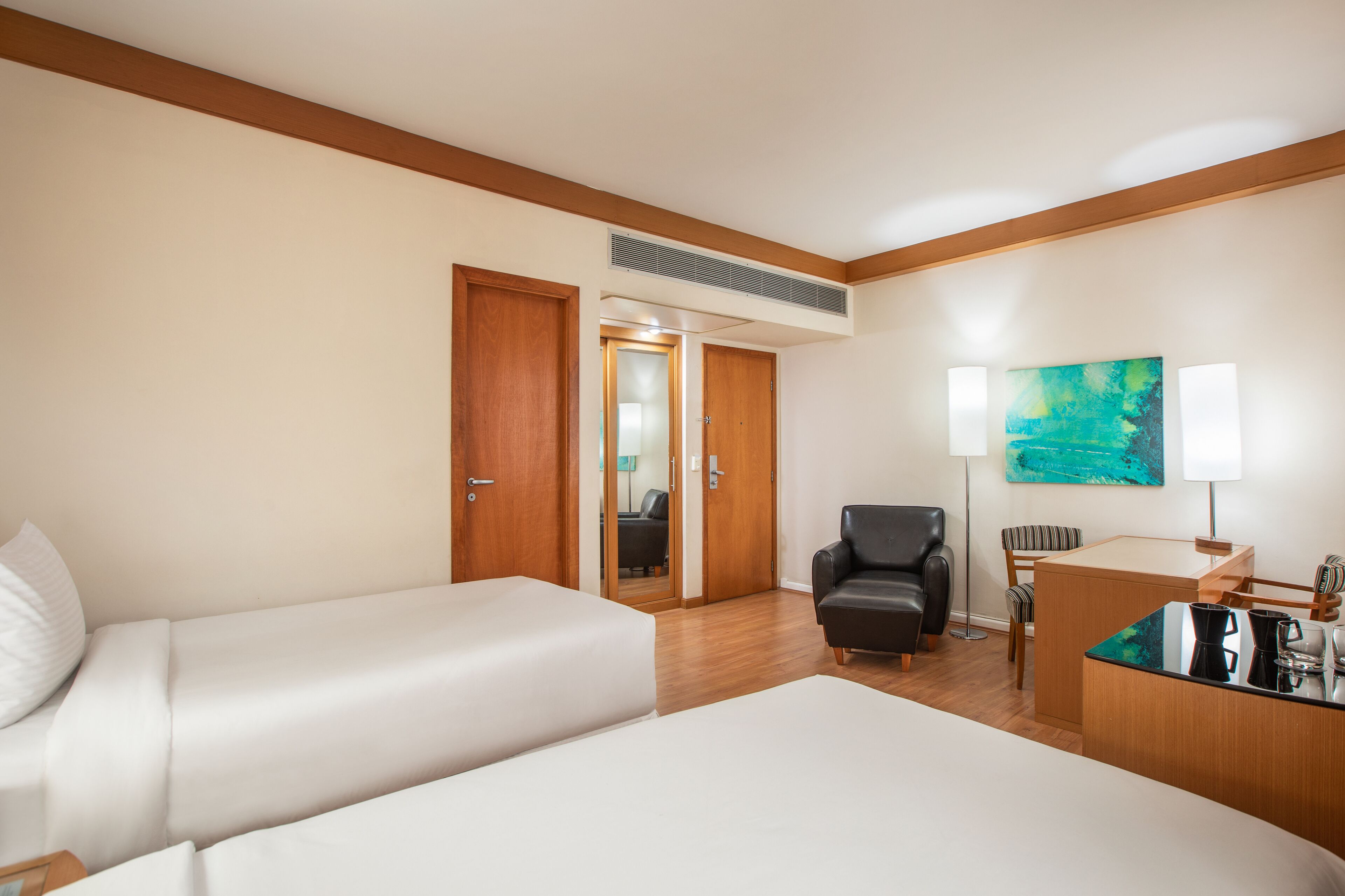 A hotel room with two beds, a desk, a chair, and a painting on the wall.